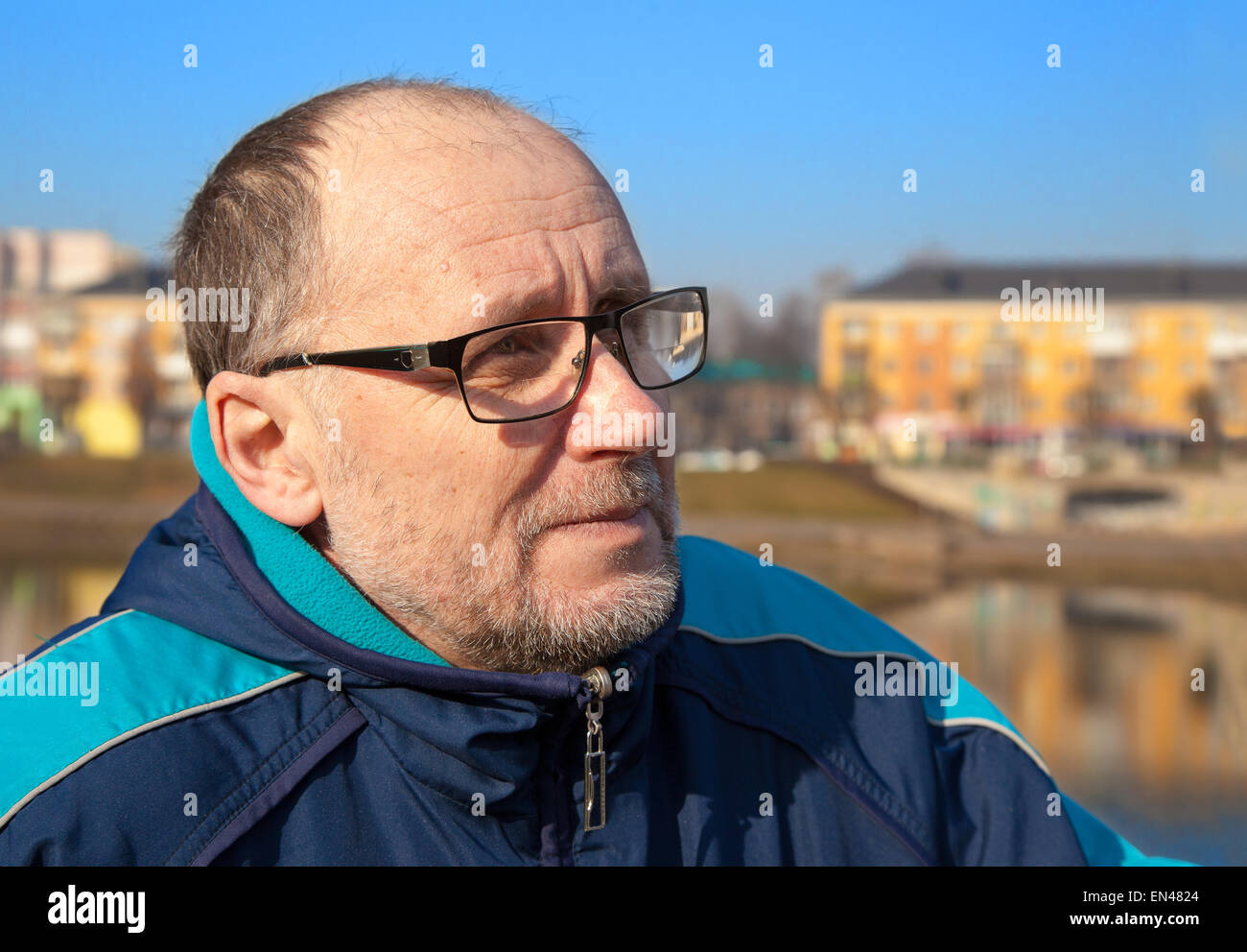 Porträt der ältere Mann mit Brille und eine blaue Jacke in einem Stadtpark Stockfoto