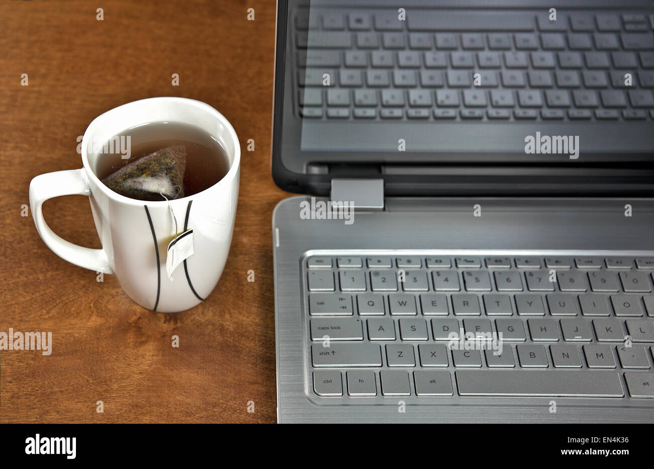 Teebeutel in heißes Wasser mit Laptop auf Holztisch. Stockfoto