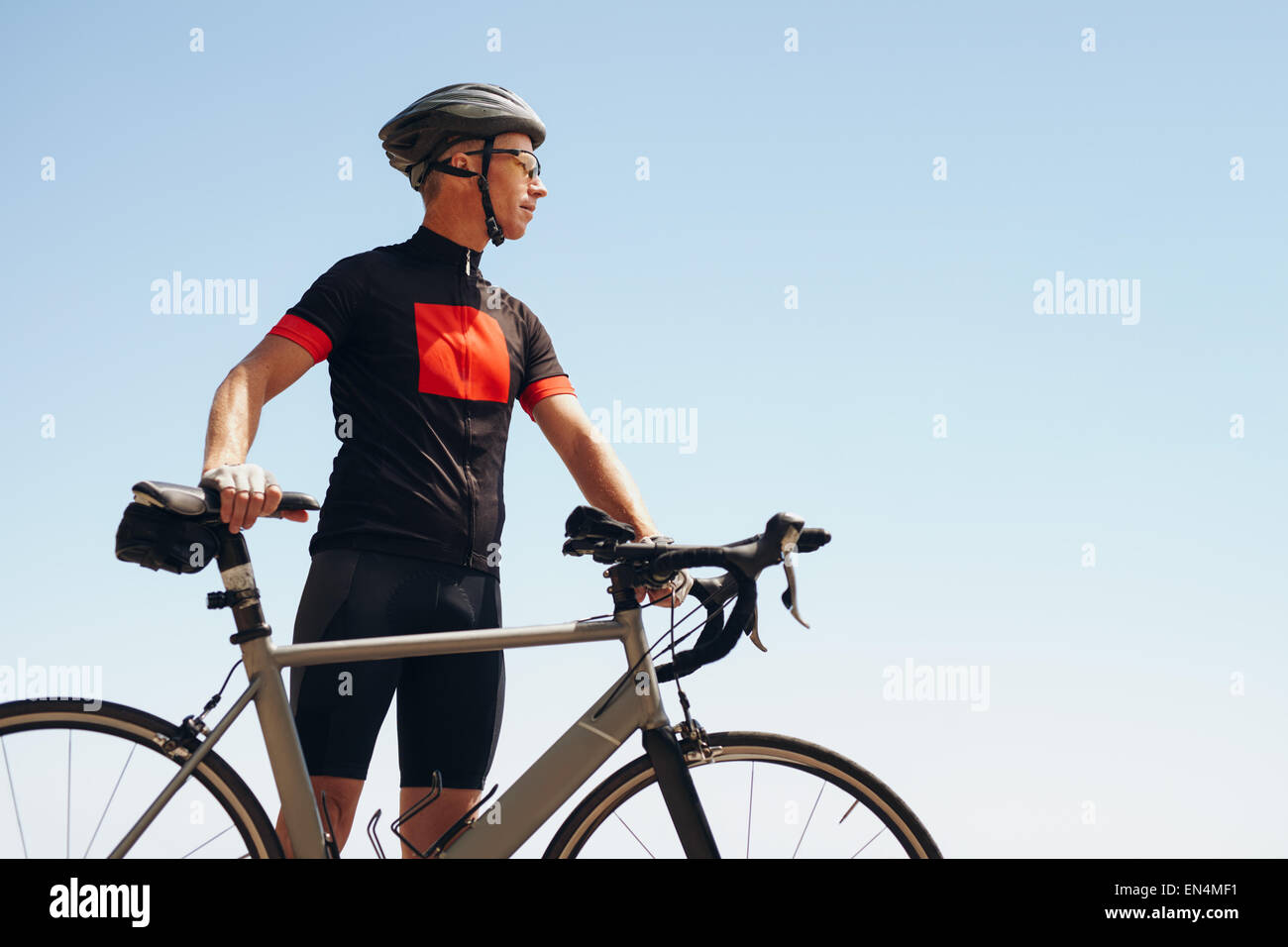 Bild des ermittelten männlichen Radfahrer wegsehen stehend gegen Himmel. Fit Mann tragen Sportswear und Radfahren Helm suchen Stockfoto