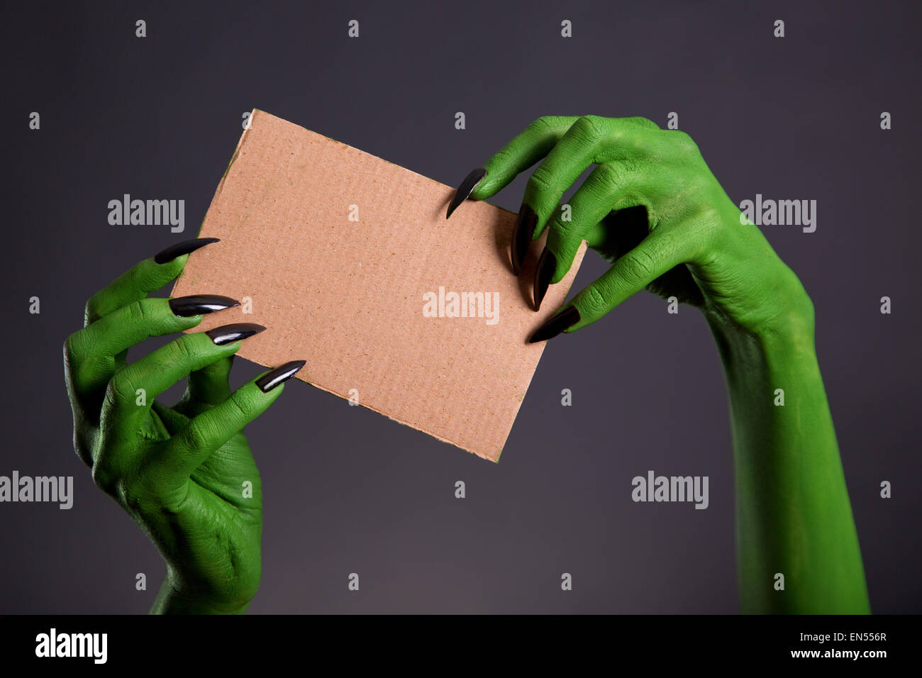 Grüne Hände mit langen schwarzen Nägeln mit leeren Stück Pappe, Halloween-Thema Stockfoto
