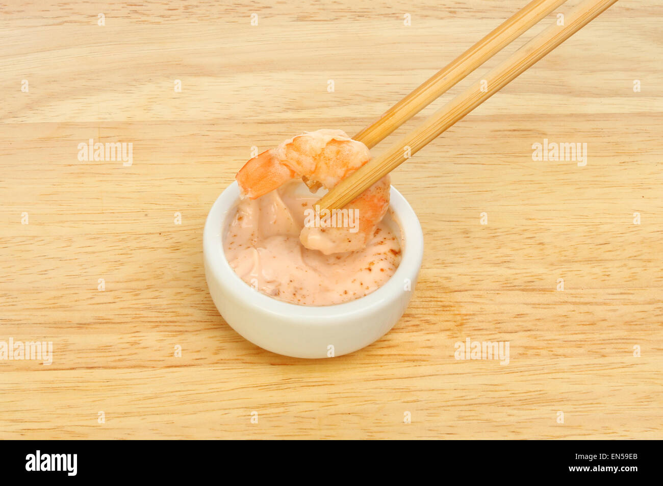 Kingsize-Garnelen in Stäbchen eintauchen in Meeresfrüchte-Sauce in ein Töpfchen auf einem Holzbrett Stockfoto