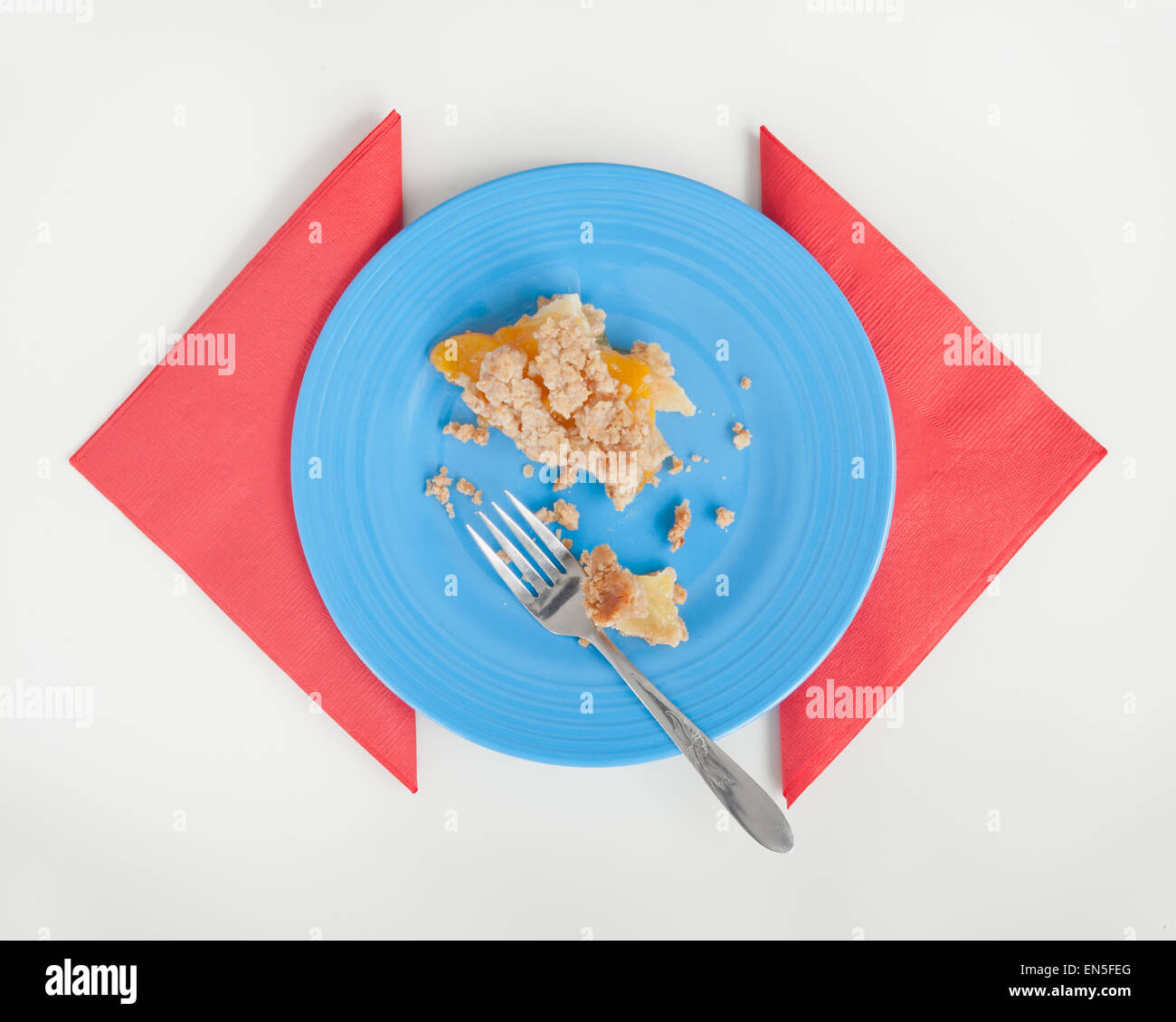 Pfirsich-Streusel Kuchen Reste auf der blauen Platte mit roten Servietten. Weiße Tischplatte. Stockfoto