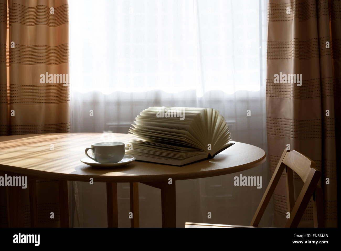 Aufgeschlagene Buch und einer Tasse Heißgetränk auf einem Tisch Stockfoto