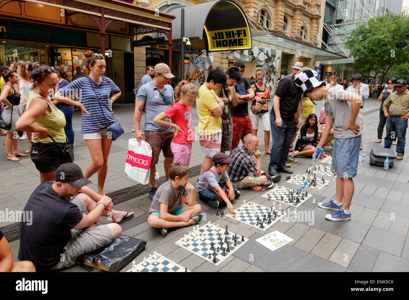 Junger Mann in einer verkehrsberuhigten Straße Simultanschach mit mehreren Personen zu spielen, während andere zusehen. Outdoor-Brettspiel; im freien; Publikum Stockfoto