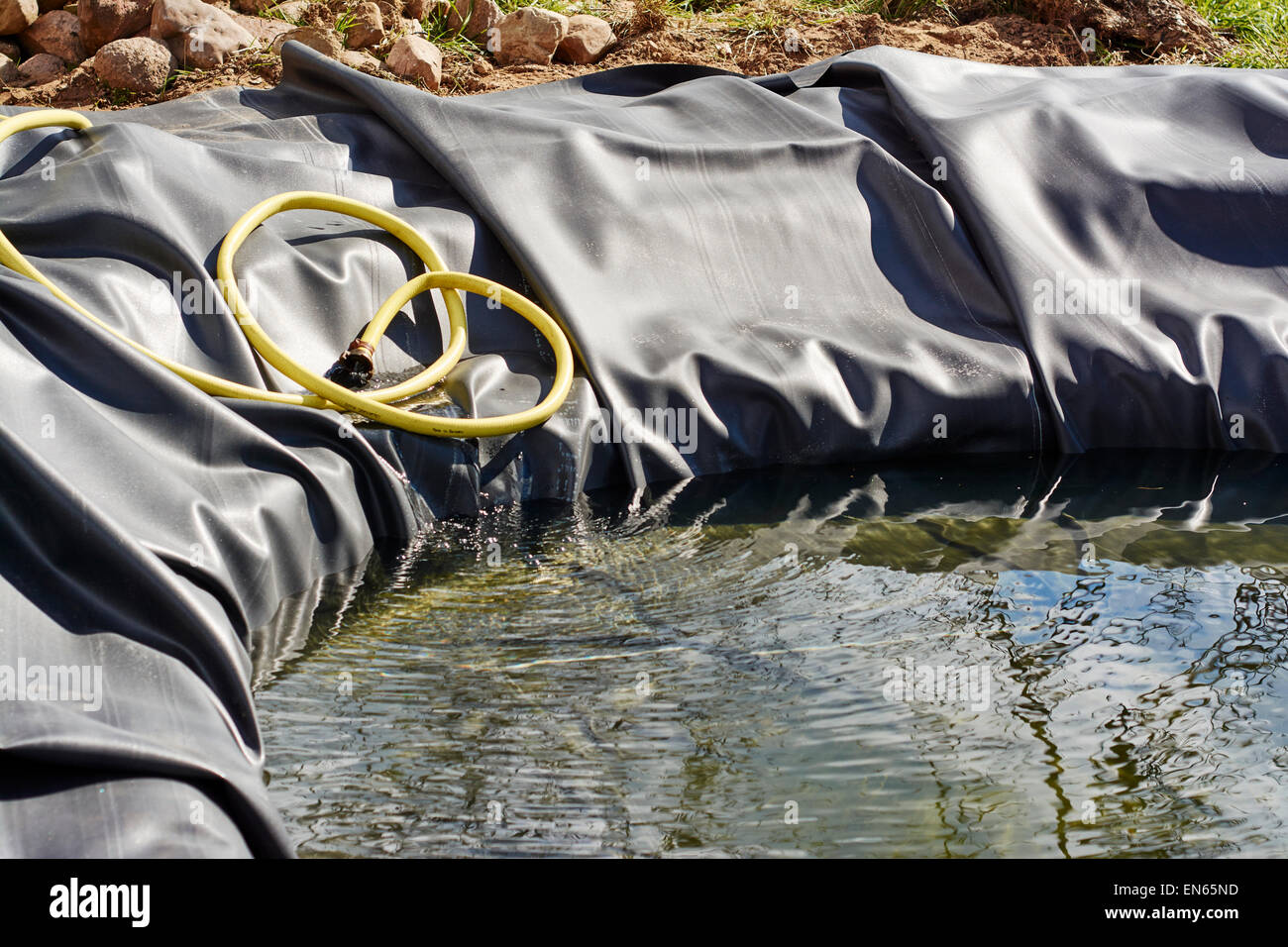 Neuen Teich mit Kautschuk-Einlage wird zum ersten Mal mit Wasser gefüllt. Stockfoto