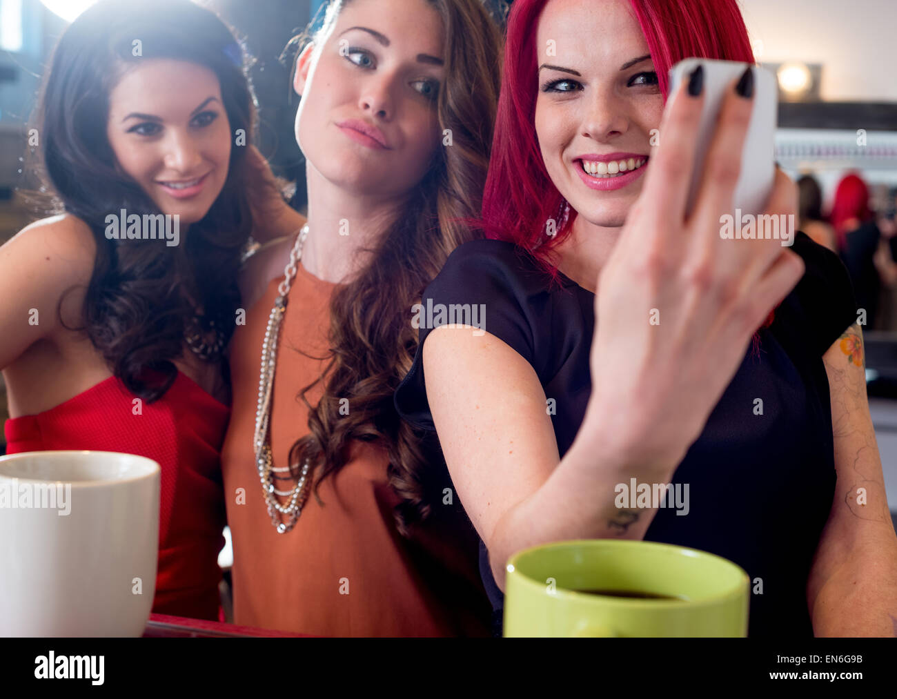 Drei junge modebewusste Frauen Kaffee-Bar auf der Suche und lachen während der Einnahme von Selfie mit Handy Stockfoto