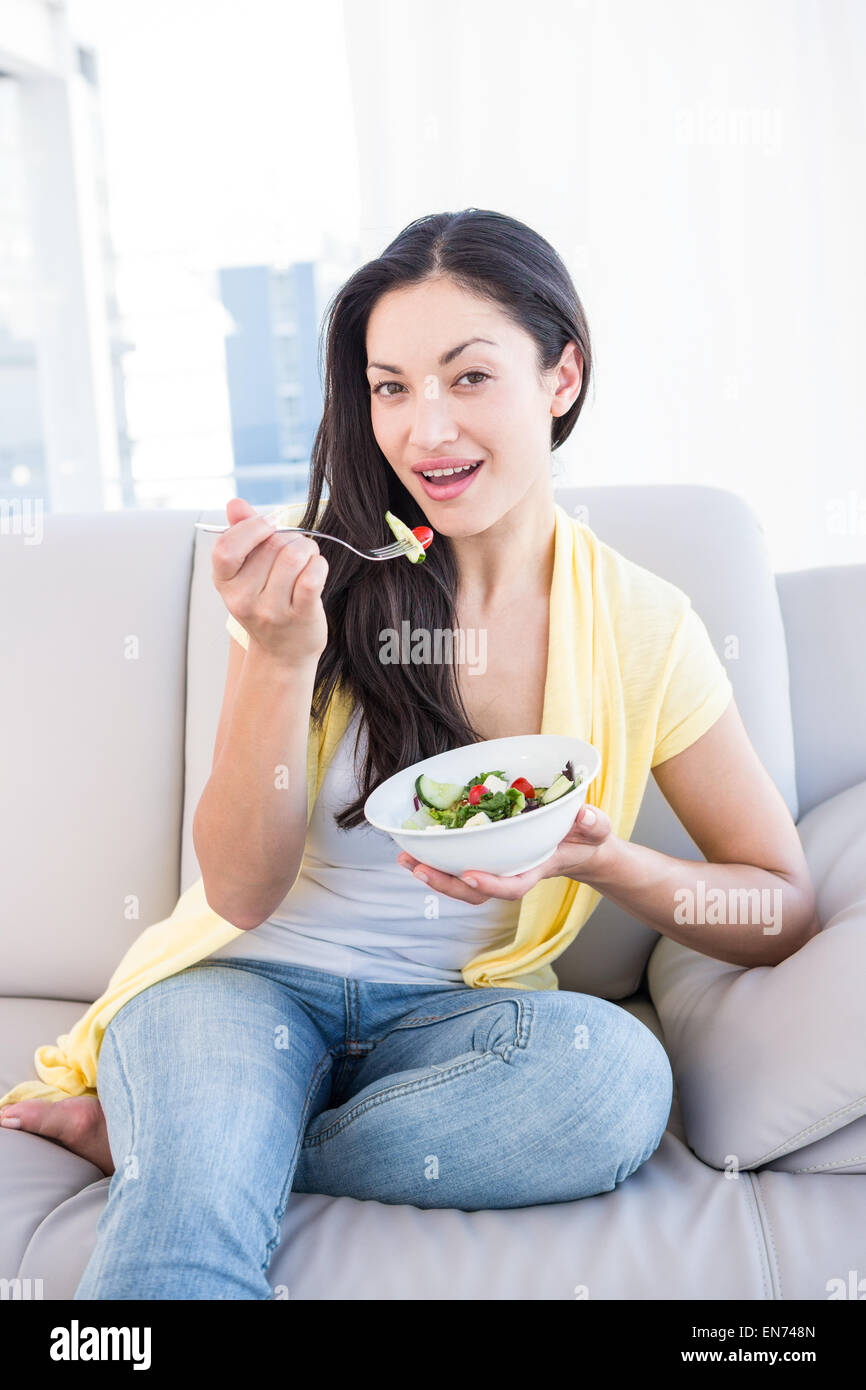 Hübsche Brünette Blick in die Kamera und essen Salat auf couch Stockfoto