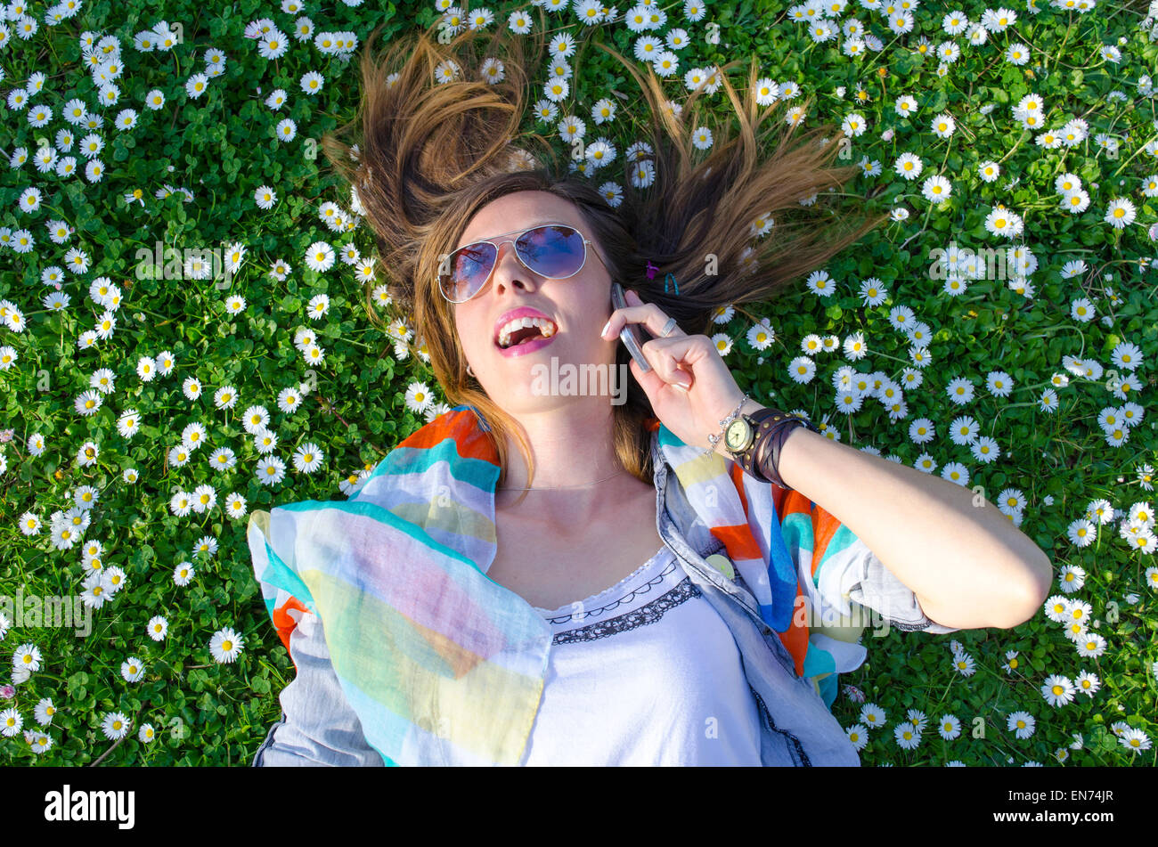Brünette Mädchen am Telefon in der Wiese mit Blumen umgeben Stockfoto