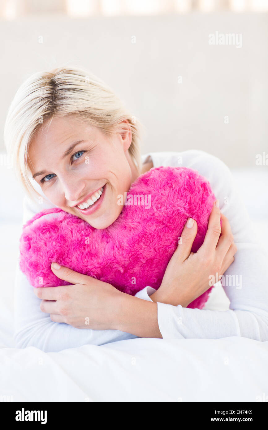 Lächelnde blonde Frau mit Herz Kissen Stockfoto