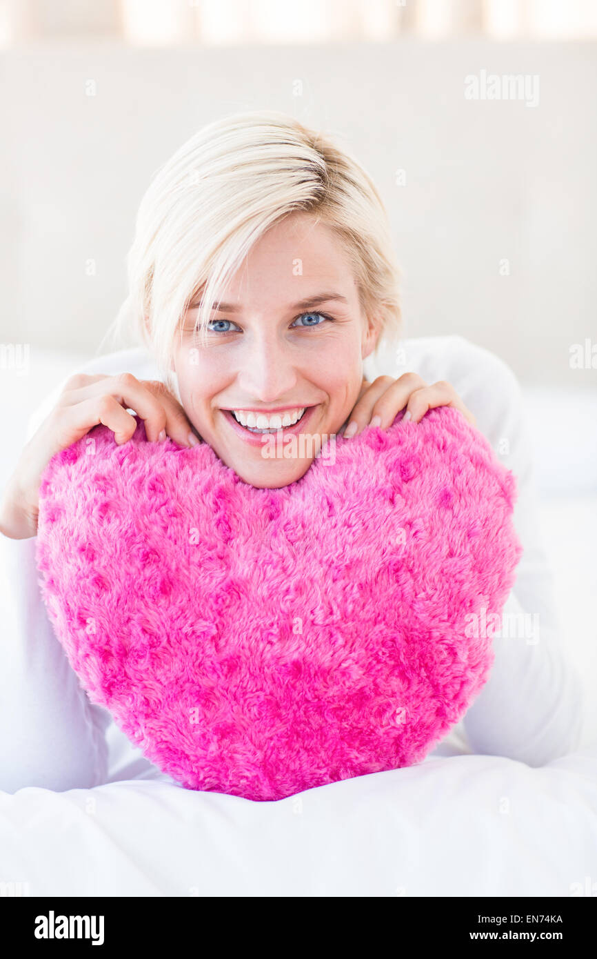 Lächelnde blonde Frau mit Herz Kissen Stockfoto