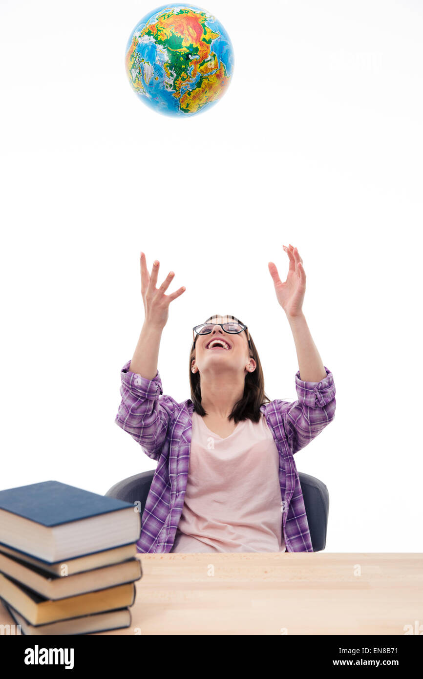 Glückliche Studentin am Tisch sitzen und werfen Globus in Luft auf weißem Hintergrund Stockfoto