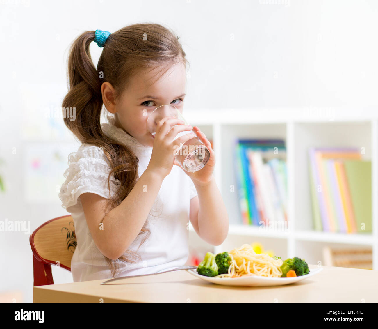 Niedliche kleine Mädchen-Trinkwasser sitzt am Tisch im Kindergarten Stockfoto