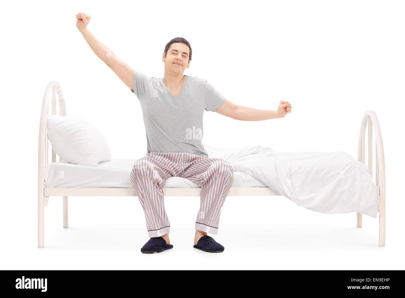 Fröhlicher Mensch aufwachen aus dem Schlaf und stretching sitzen auf seinem Bett isoliert auf weißem Hintergrund Stockfoto