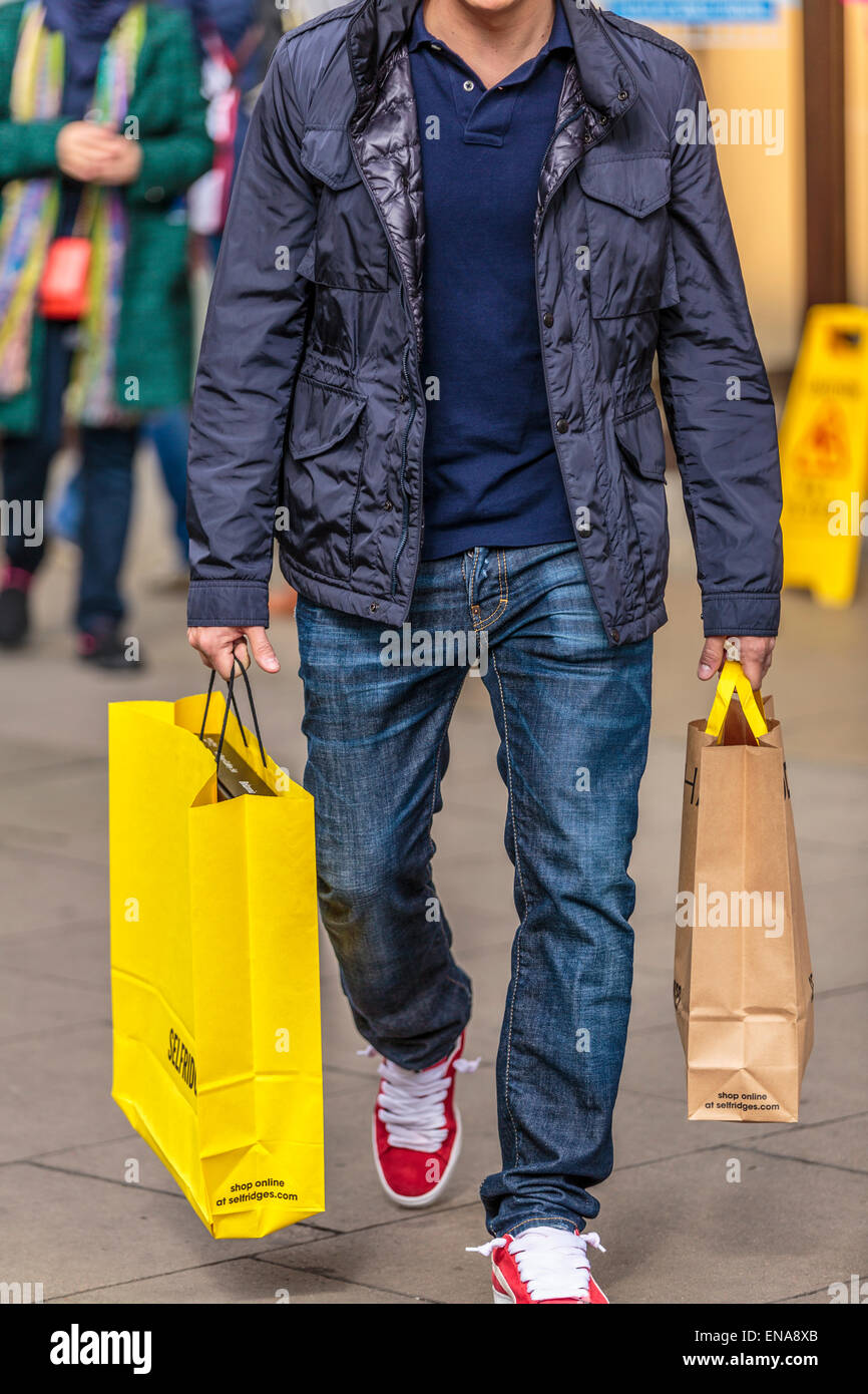Ein Porträt eines jungen Mannes wandern mit mehreren Einkaufstüten in der Hand London England Großbritannien Stockfoto