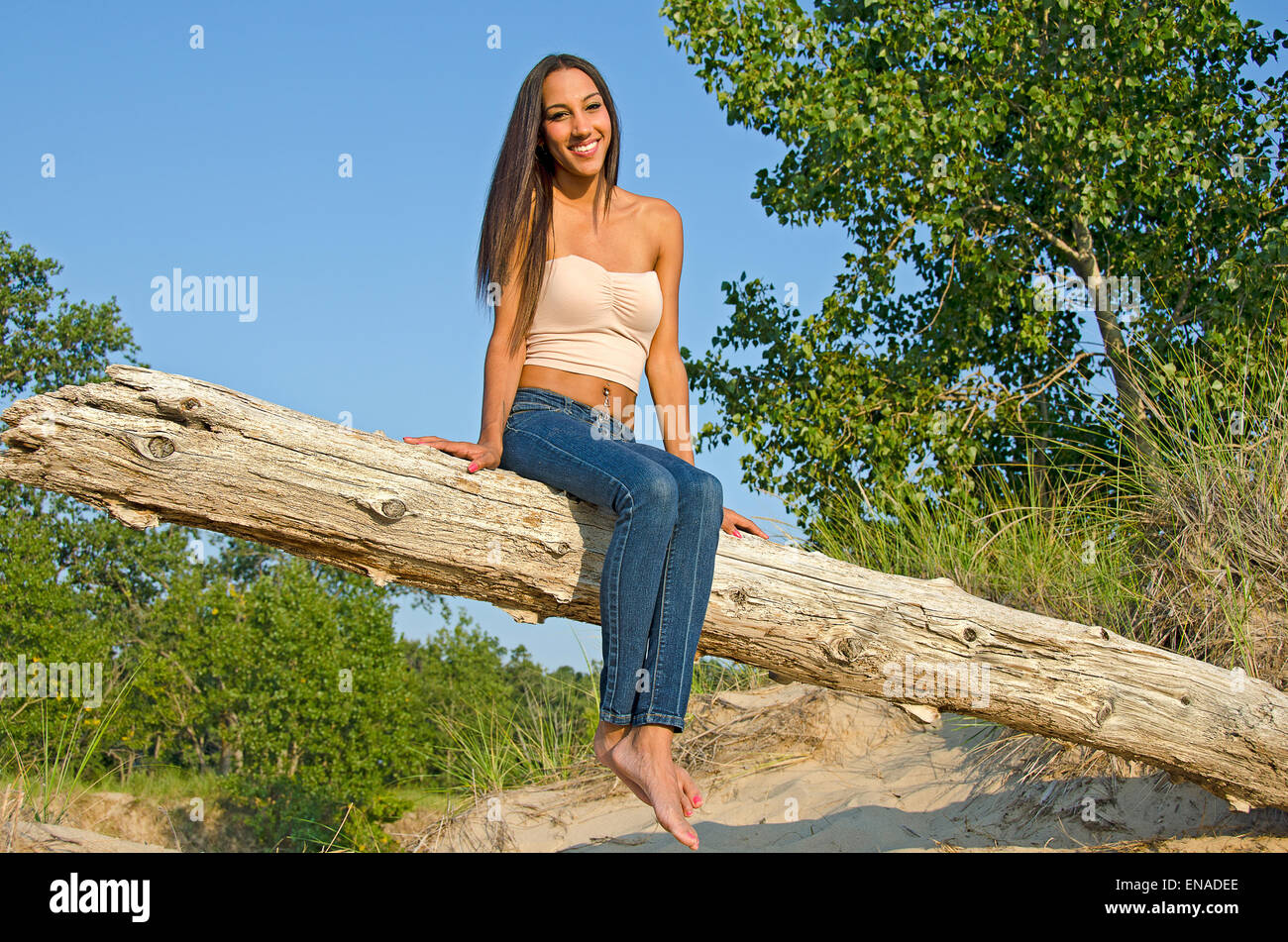 Schöne lächelnde junge Brünette Frau stellte auf einem Baumstamm. Stockfoto