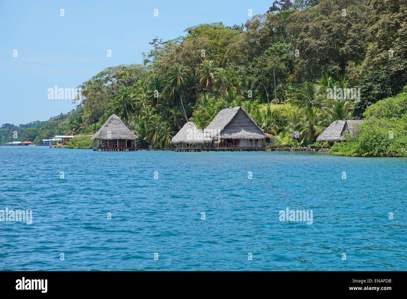 Öko-Lodge mit strohgedeckten Hütten über dem Wasser und üppiger tropischer Vegetation auf der karibischen Küste von Panama, Bocas del Toro Stockfoto