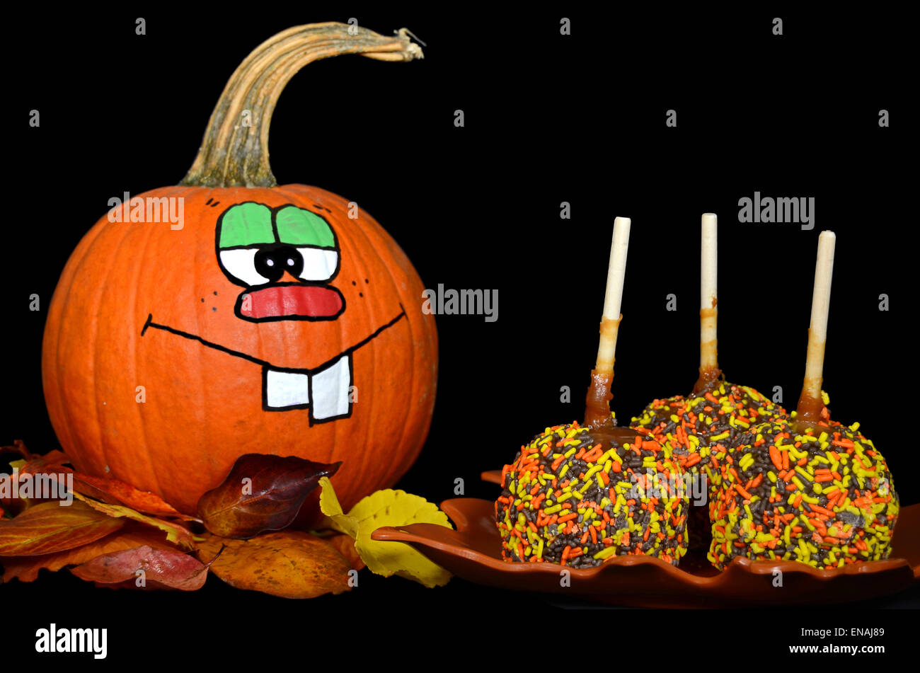 Lustiges Gesicht gemalt auf einem Herbst-Kürbis mit Süßigkeiten Streusel auf Äpfel mit Karamell. Stockfoto
