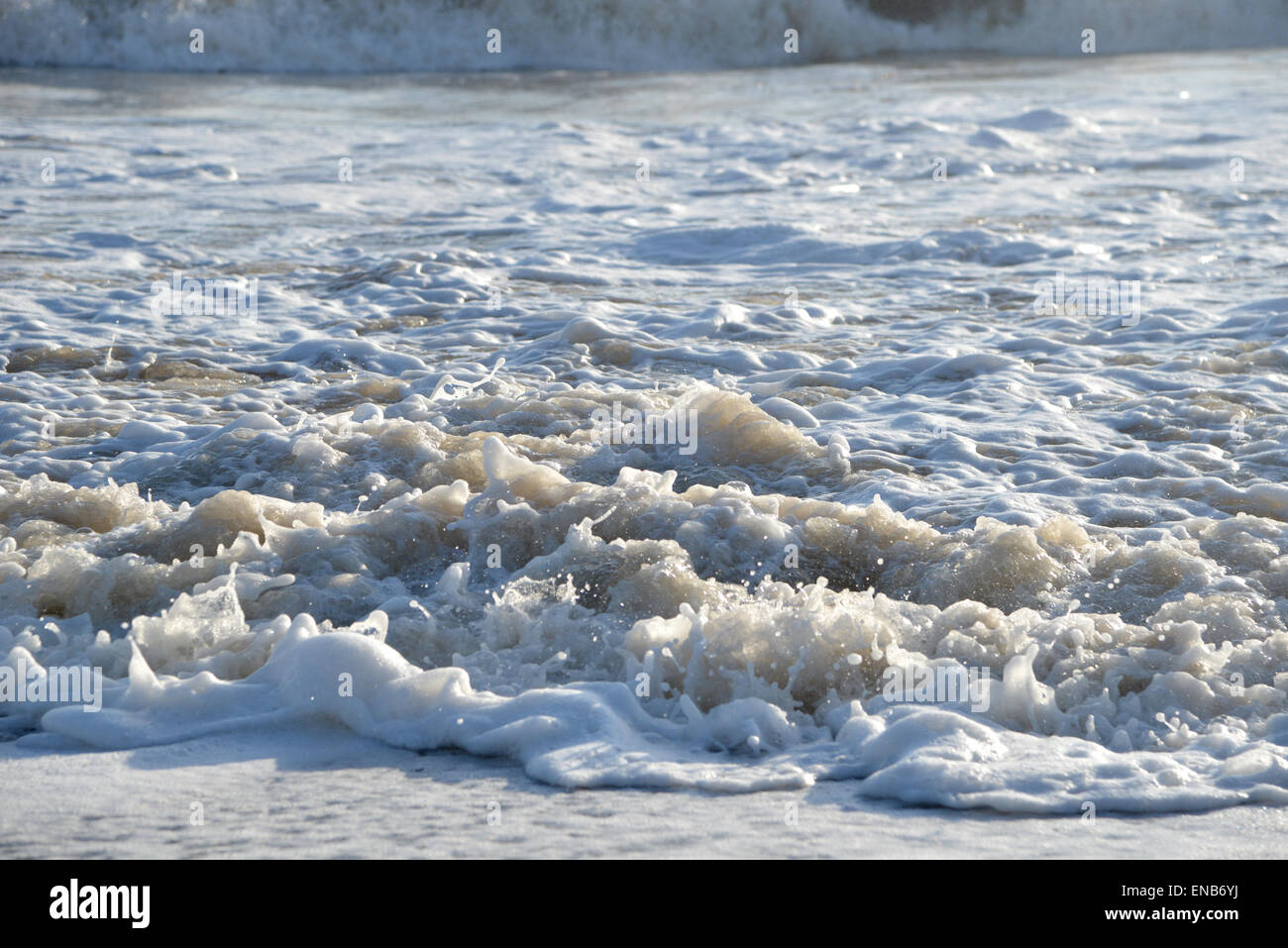 Weißen Surf Luftblasen auf einem Sandstrand Stockfoto