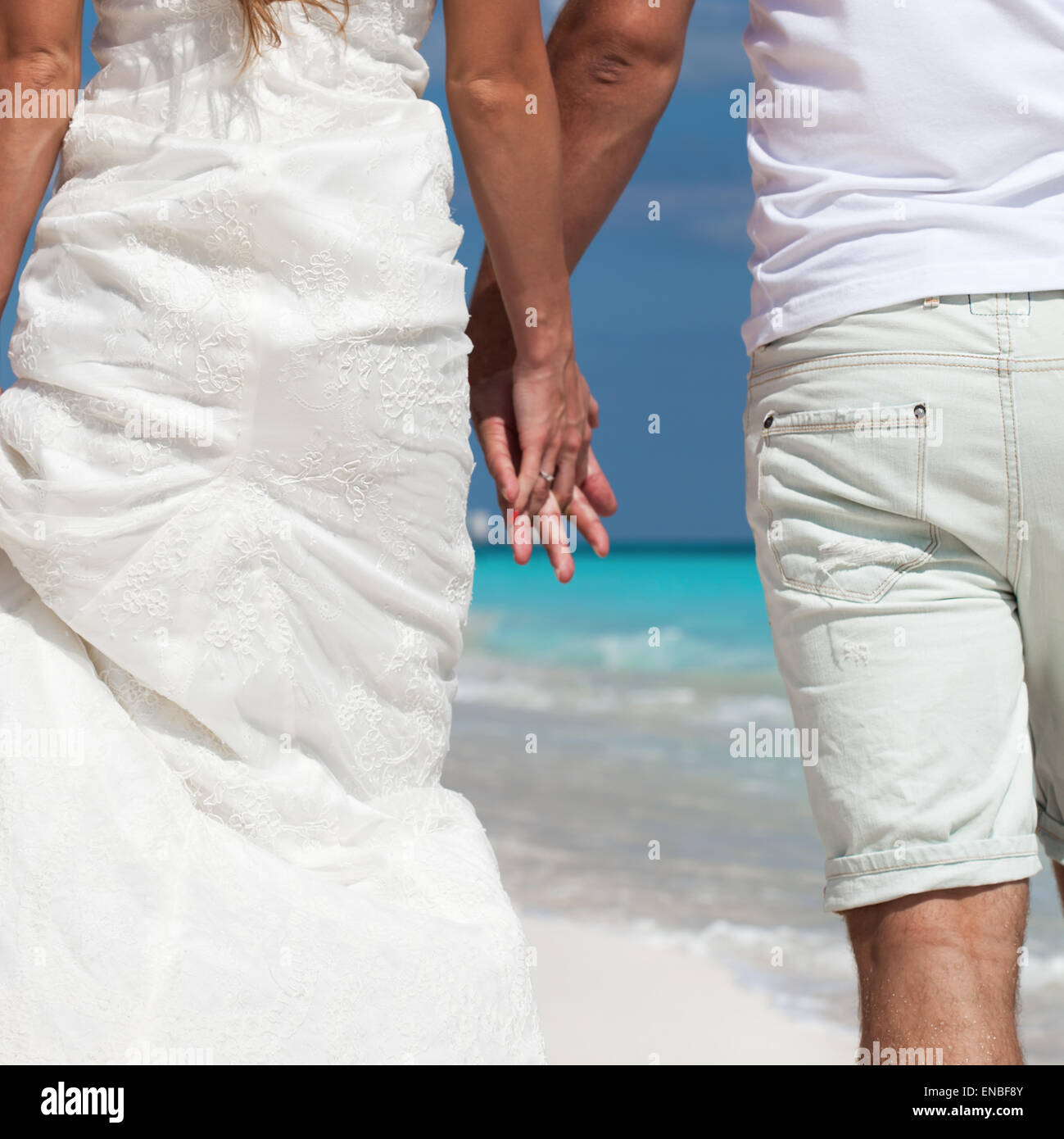 Junge schöne Brautpaar in Liebe Hand in Hand und Fuß am tropischen Sandstrand, Ansicht von hinten Stockfoto