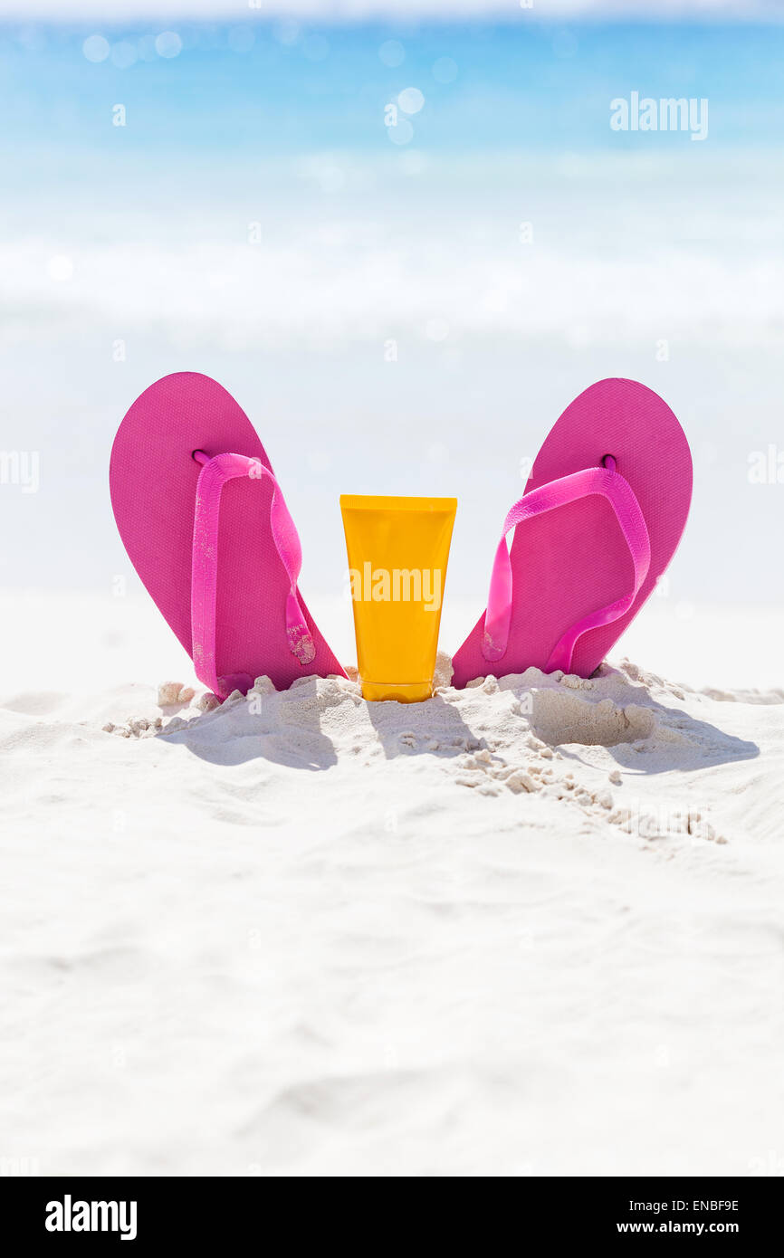 Rosa lebhaften Strand Flip-Flops mit Sonnencreme Schutz Gesichtscreme im weißen Sand am Meer-Hintergrund. Tropischer Sommer Urlaub con Stockfoto