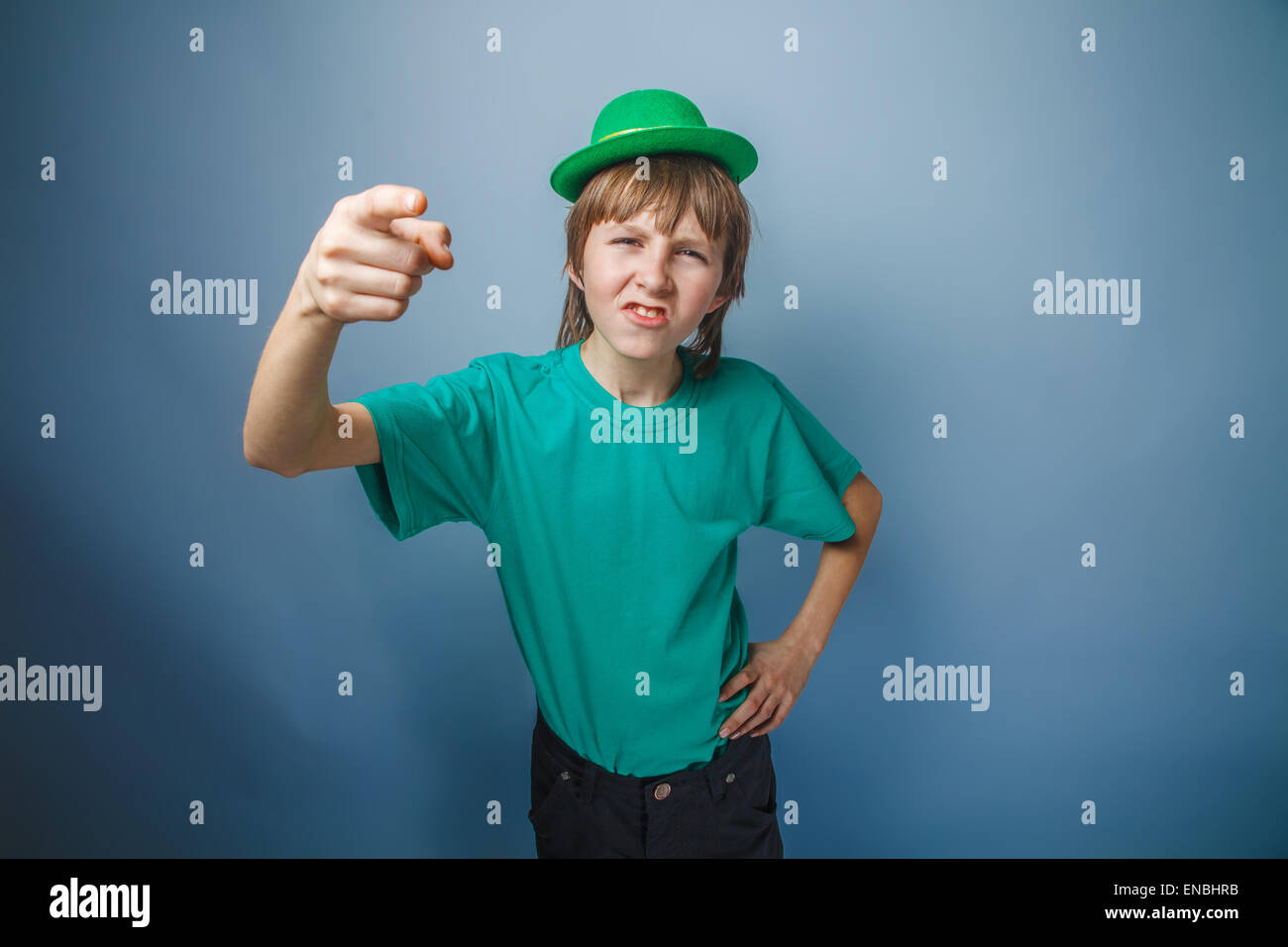 Spotten Sie junge Teenager europäischen Auftritt im grünen Hut zeigt seinen Finger nach vorne auf einem grauen Hintergrund, Stockfoto