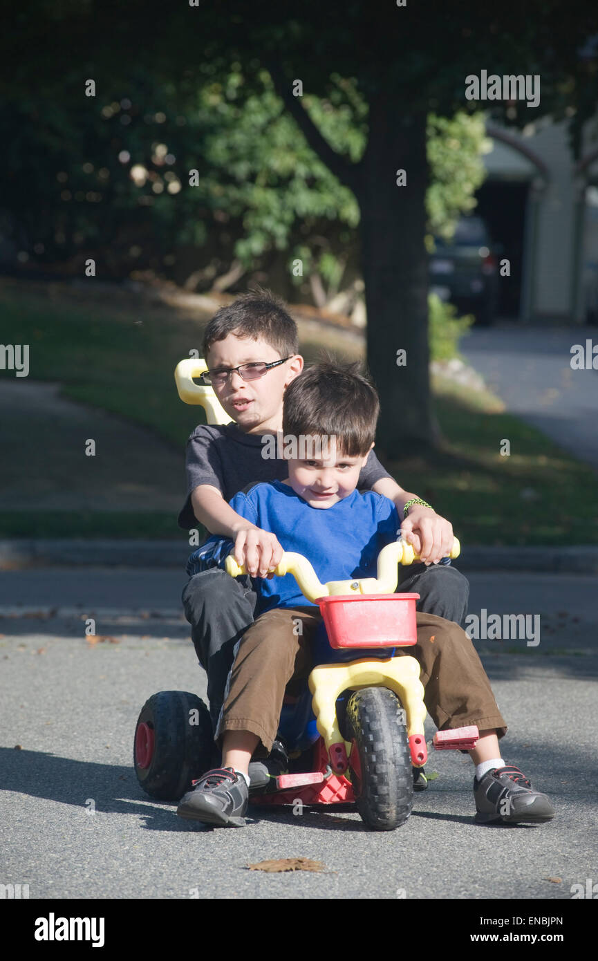 Zwei Brüder, Alter von sieben und vier fahren einen großes Rad drei Wheeler in ihrer Einfahrt. Stockfoto