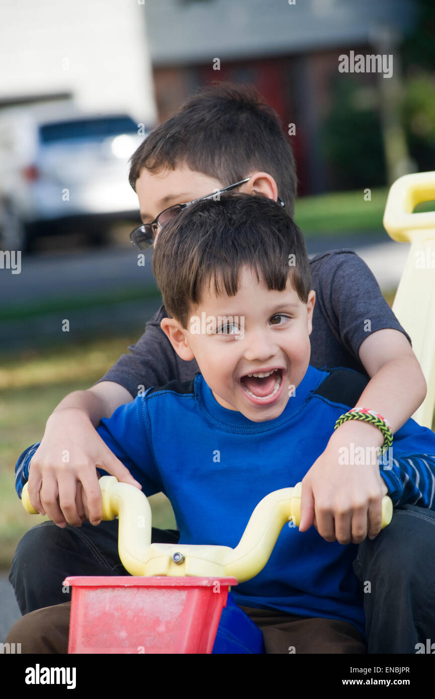 Zwei Brüder, Alter von sieben und vier fahren einen großes Rad drei Wheeler in ihrer Einfahrt. Stockfoto