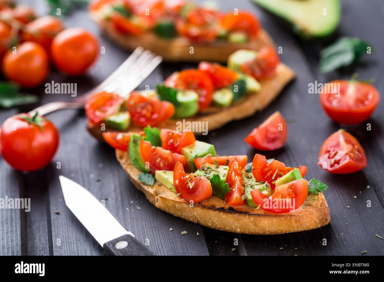 Bruschetta mit Tomaten, Avocado und Kräuter auf einem schwarzen Holztisch Stockfoto