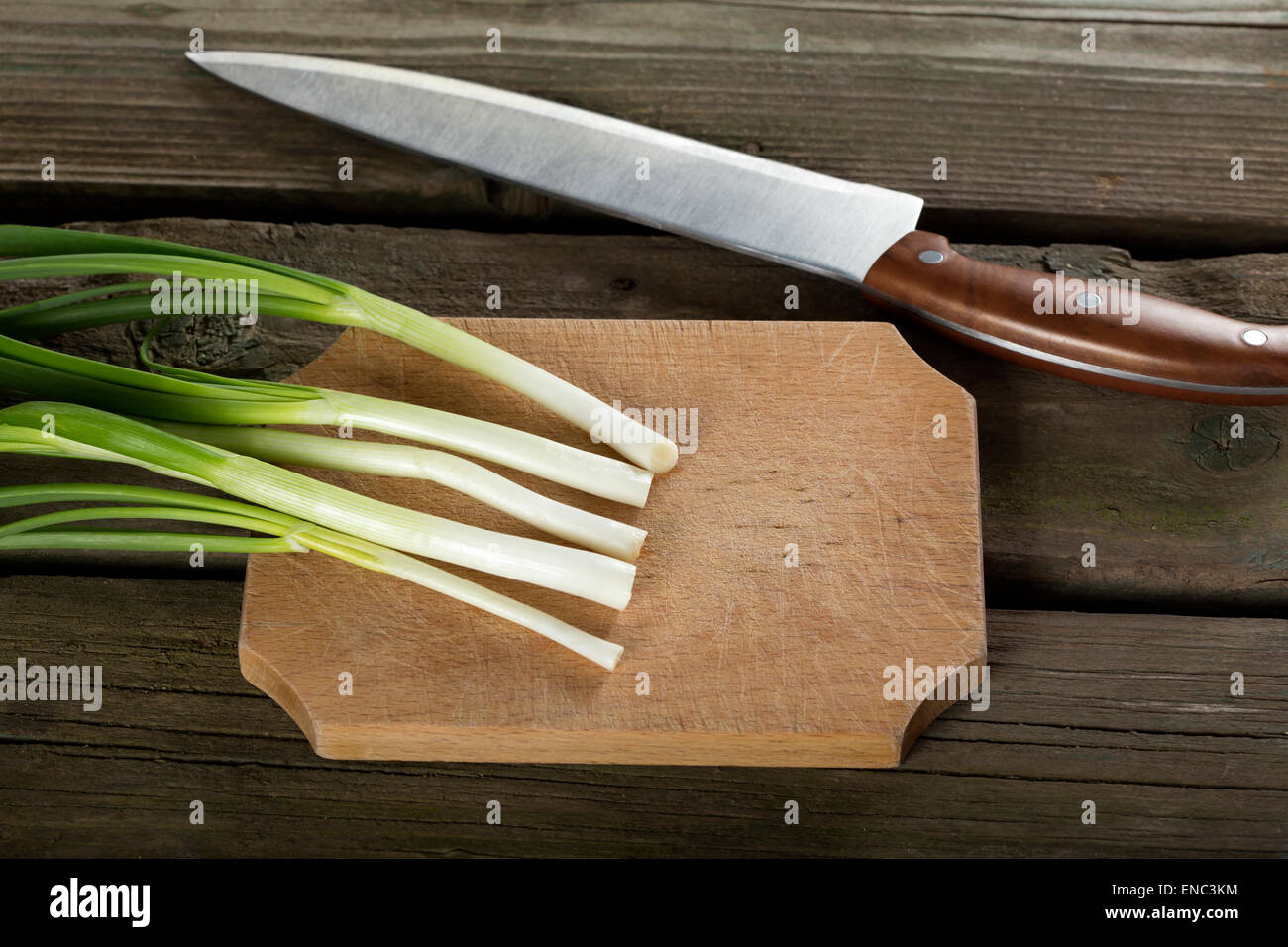 grüne Zwiebeln auf einem Holzbrett und einem Küchenmesser Stockfoto