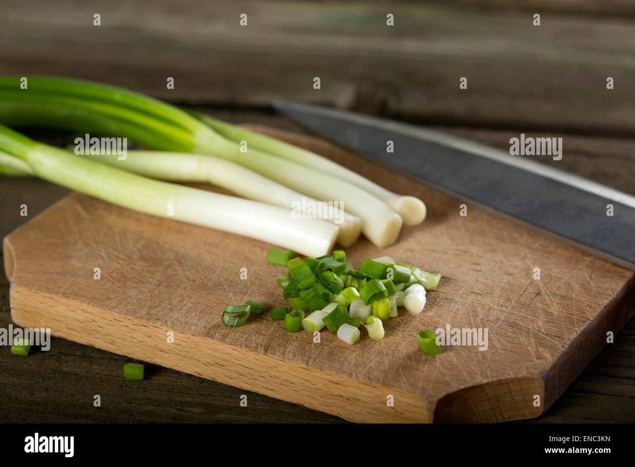 Grüne Zwiebeln schneiden auf einem Holzbrett mit Küchenmesser Stockfoto