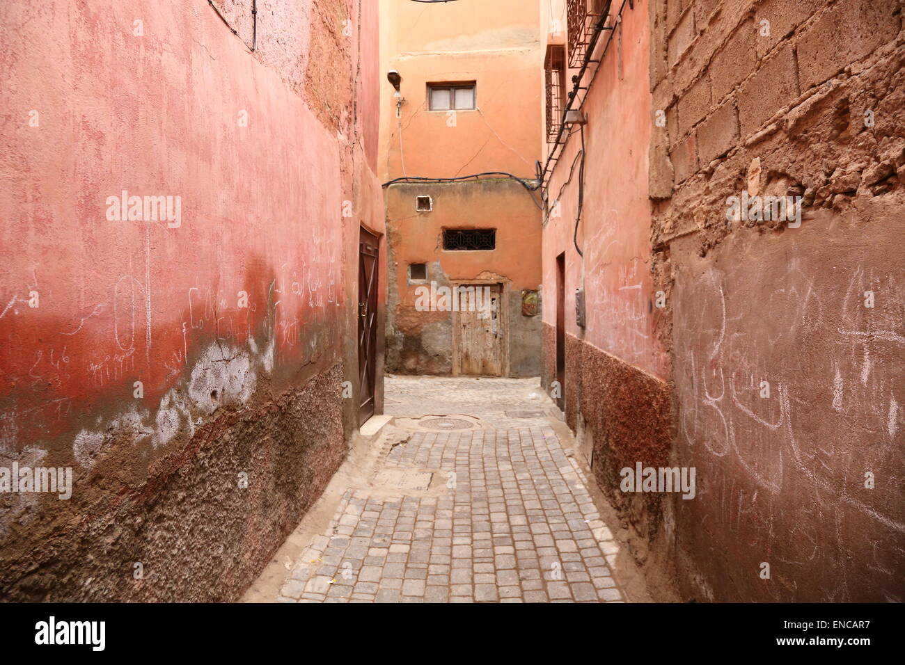 Rote Wände, eine Tür und Kreide Graffiti in einer schmalen Seitenstraße in der Medina, Marrakesch, Marokko Stockfoto