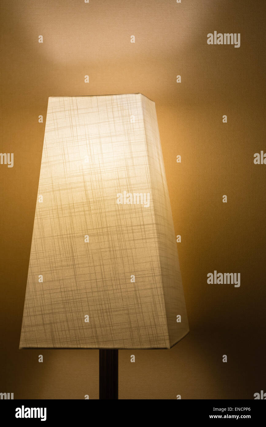 Eine Lampe mit einem Stoff-Lampenschirm in einem dunklen Raum gegen eine einfache Wand. Stockfoto