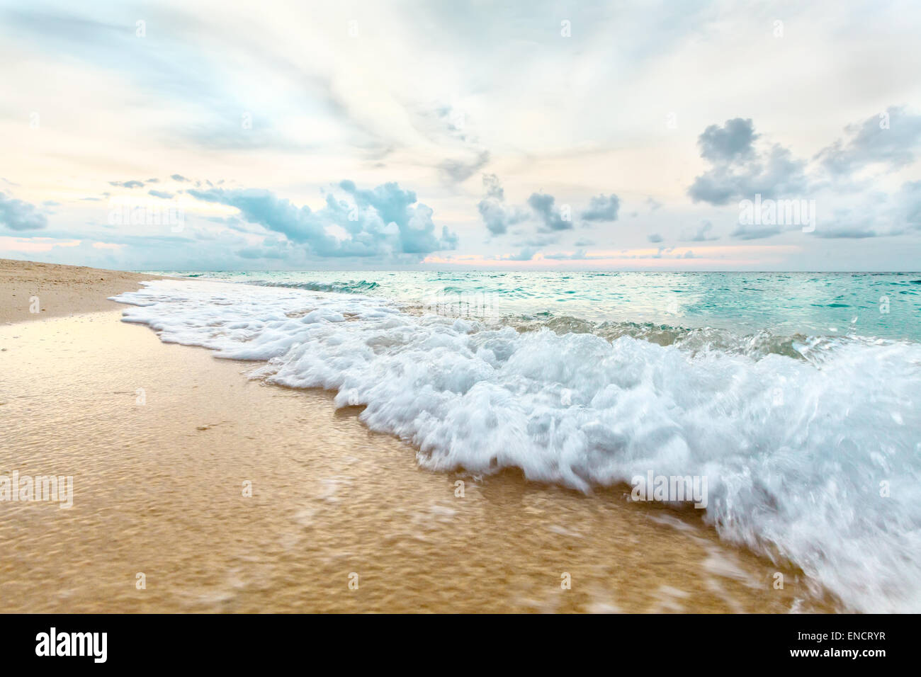 Weiße Wellen mit Luftblasen auf gelben Sandstrand des blauen Meeres auf Sonnenuntergang Stockfoto