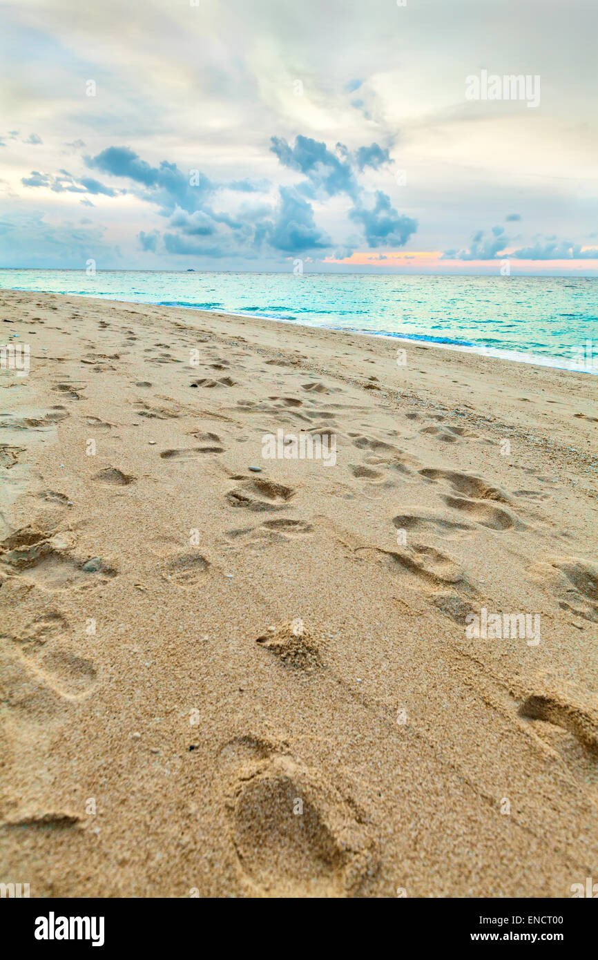 Spuren im gelben Sandstrand auf der tropischen Insel in der Nähe von Meer bei Sonnenuntergang Stockfoto