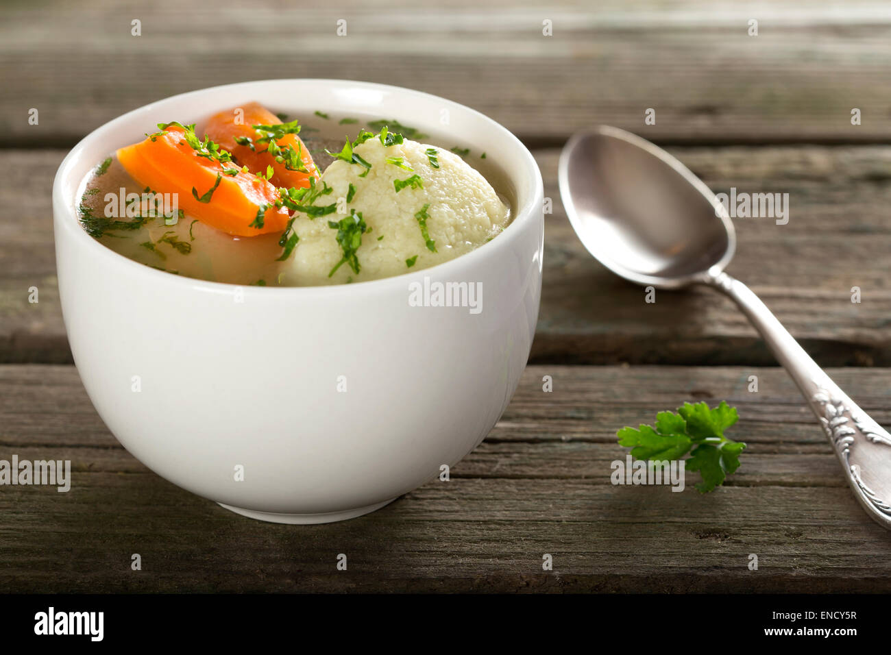 Traditionelle Hühnersuppe mit Knödel auf einem rustikalen Holztisch mit silbernen Löffel Stockfoto