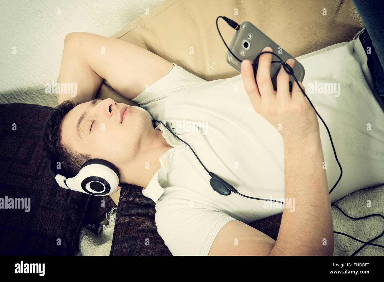 Mann auf der Couch halten Smartphone Musikhören mit Kopfhörer Tagträumen Stockfoto