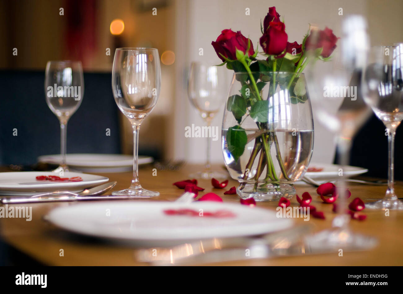 Ein Esstisch set mit Maßgedecke, Weingläser & rote Rosen in einer Vase für eine Feier Mahlzeit Stockfoto