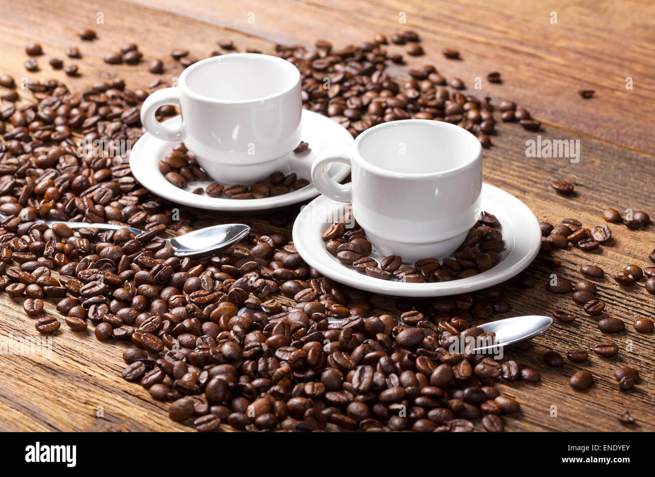 Zwei leere Kaffeetassen und Löffel unter Kaffeebohnen auf einem Holztisch. Stockfoto