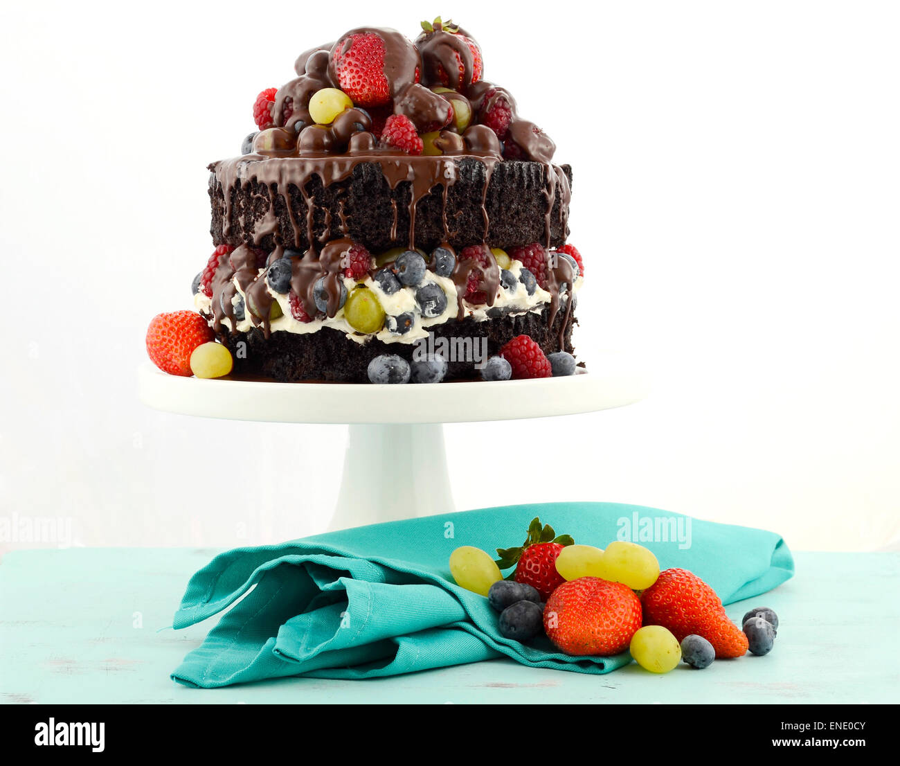 Herrlich göttlichen chocolate Cake mit Erdbeeren, Blaubeeren, Himbeeren und Trauben und Creme auf blass blauen shabby chic Reiter Stockfoto