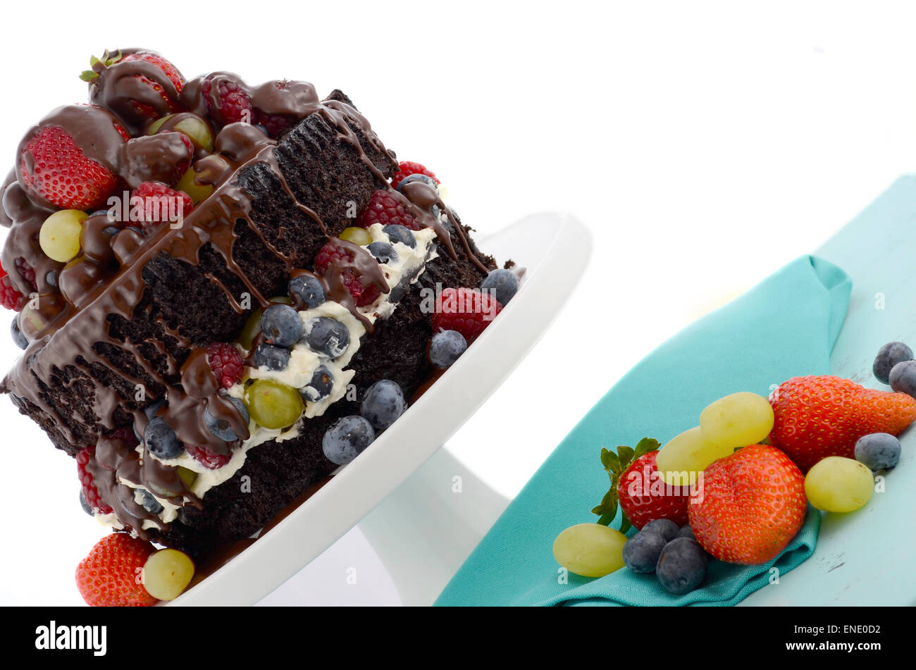 Herrlich göttlichen chocolate Cake mit Erdbeeren, Blaubeeren, Himbeeren und Trauben und Creme auf blass blauen shabby chic Reiter Stockfoto