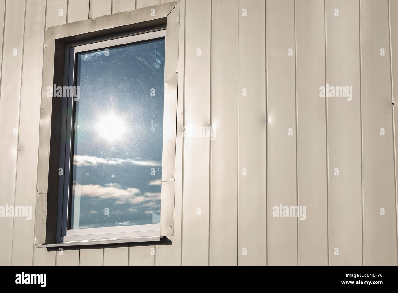 Fenster mit Reflektion der Sonne in hellgelber Farbe Kunststoff siding Paneele Wand Stockfoto