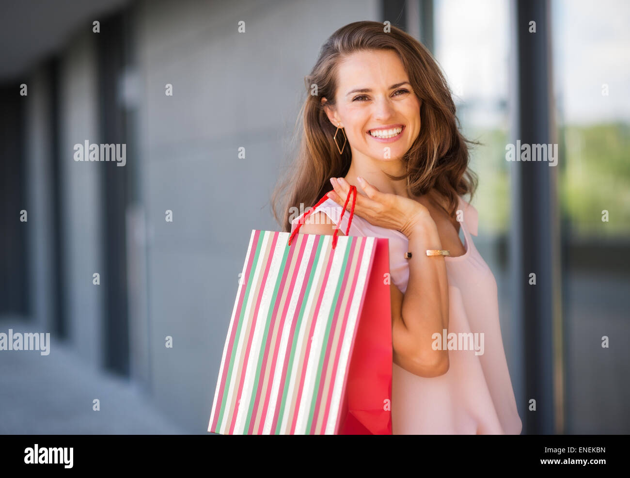 Eine Braunhaarige Frau ist von der Taille bis gesehen. Sie hält eine gestreifte, bunte und rote Einkaufstasche über ihre Rechte Schulter Stockfoto