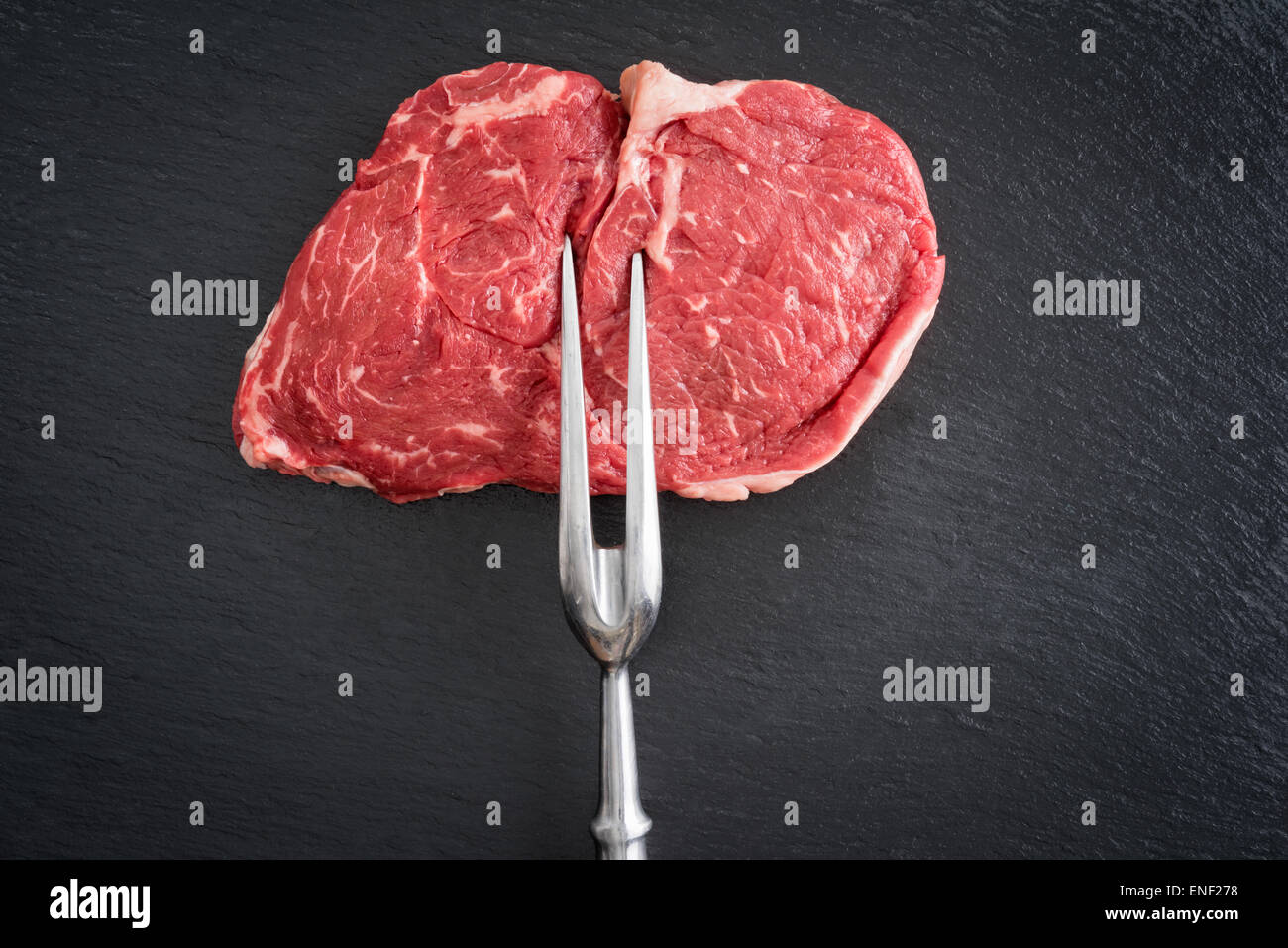 Frisches rohes Ribeye Steak mit großen Gabel auf schwarzem Hintergrund Stockfoto