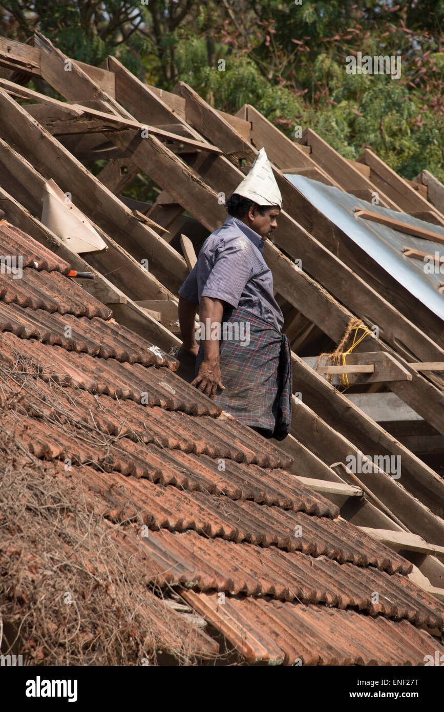 Ein Dachzieher, der einen handgefertigten Papierhut auf einem Dach eines alten Gebäudes in Fort Cochin, Kochi, Kerala, Indien trägt. Stockfoto