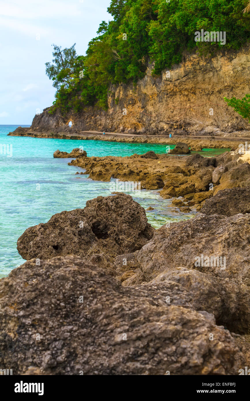 Blick auf das Meer mit großen Felsen am vorderen Hintergrund und Felsen-Insel mit grünen Palmen Stockfoto