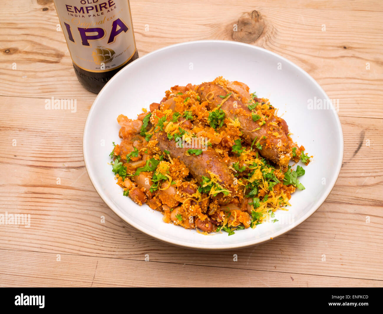 Schüssel mit französischem "Cassoulet" gemacht mit Würstchen, Bohnen und Speck mit Petersilie und Orangenschale garnieren und eine Flasche Bier IPA Stockfoto