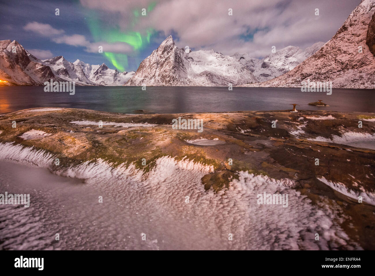 Kleine Aurora mit Wolken, Felsen und Eis, Kleinstadt und Bergen im Hintergrund, Hamnoy Island, Lofoten, Norwegen Stockfoto