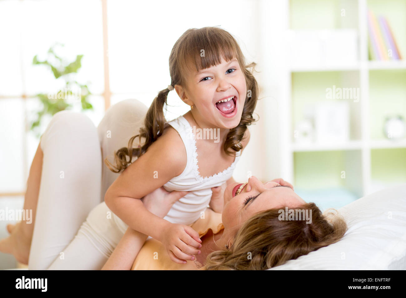 Glücklich im mittleren Alter Mutter mit der Tochter Kind im Bett im Weißen Haus Schlafzimmer spielen Stockfoto