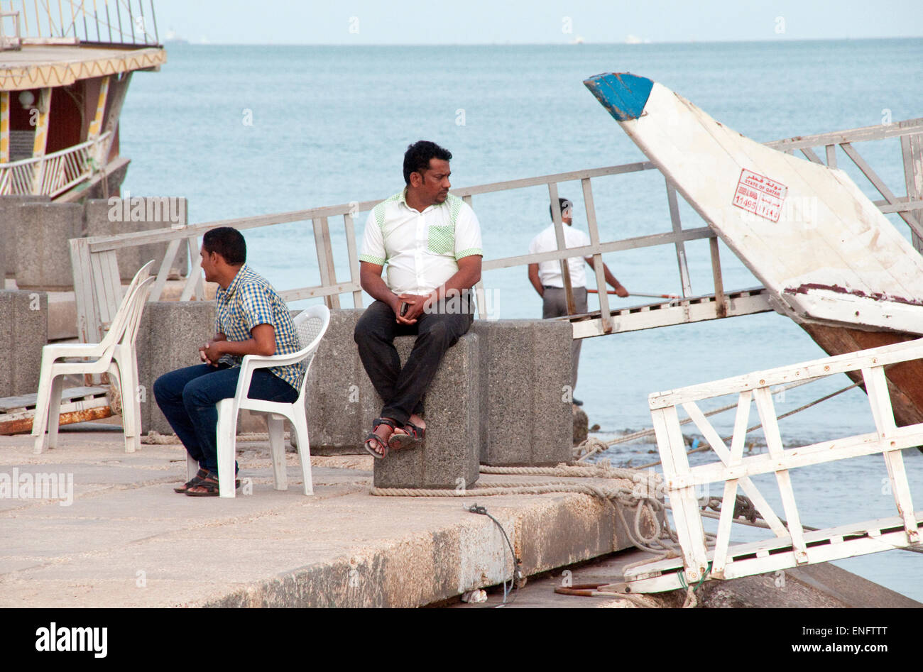 Touristischen Dhow Boot Arbeiter sitzen am Wasser durch ihre festgemachten Schiffe warten auf Passagiere, in Doha, Katar. Stockfoto