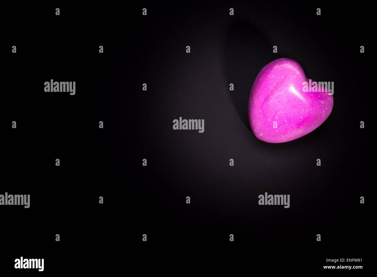 Eine beleuchtete rosa Stein Herz liegend auf schwarzem Hintergrund. Mit Exemplar Stockfoto